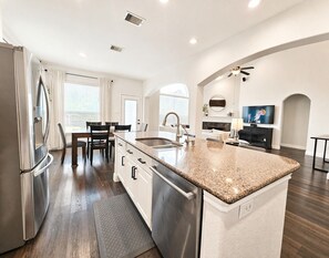 Eine moderne Küche mit einem Edelstahl-Kühlschrank, einer Granit-Arbeitsplatte und einem Essbereich mit Tisch und Stühlen.