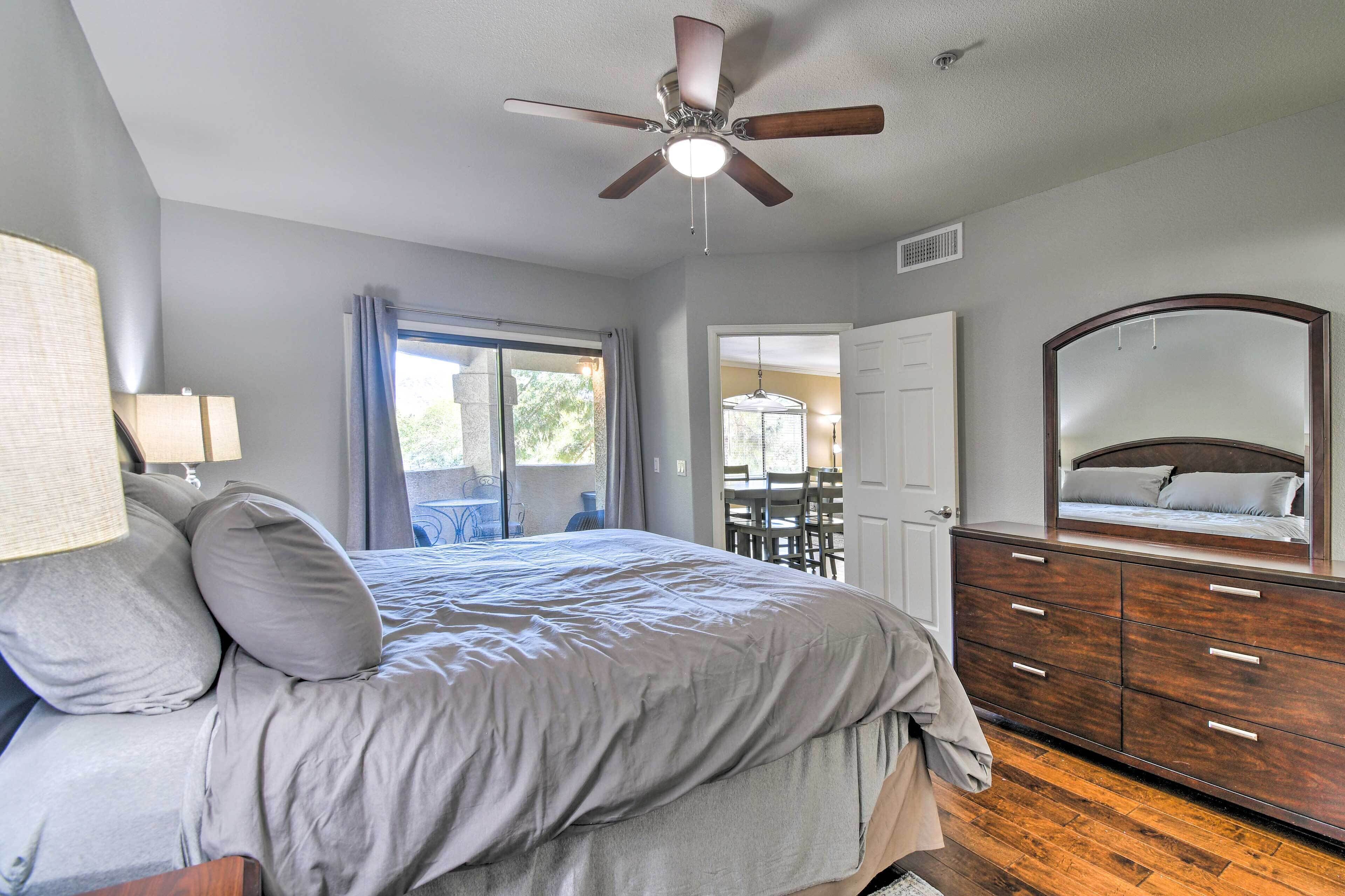 A bedroom with a bed, a dresser, a ceiling fan, a window, and a door leading to a balcony.