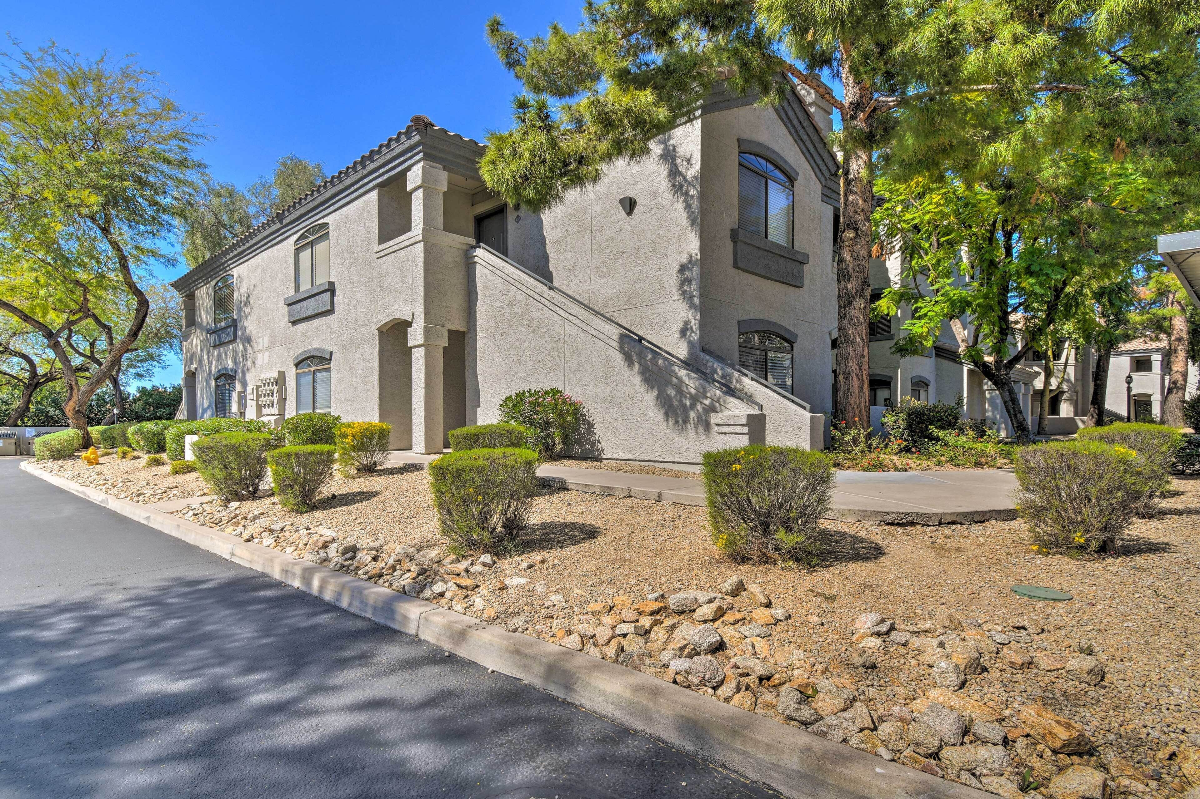 A two-story building with a stone facade, a small front garden with shrubs, and a clear sky.