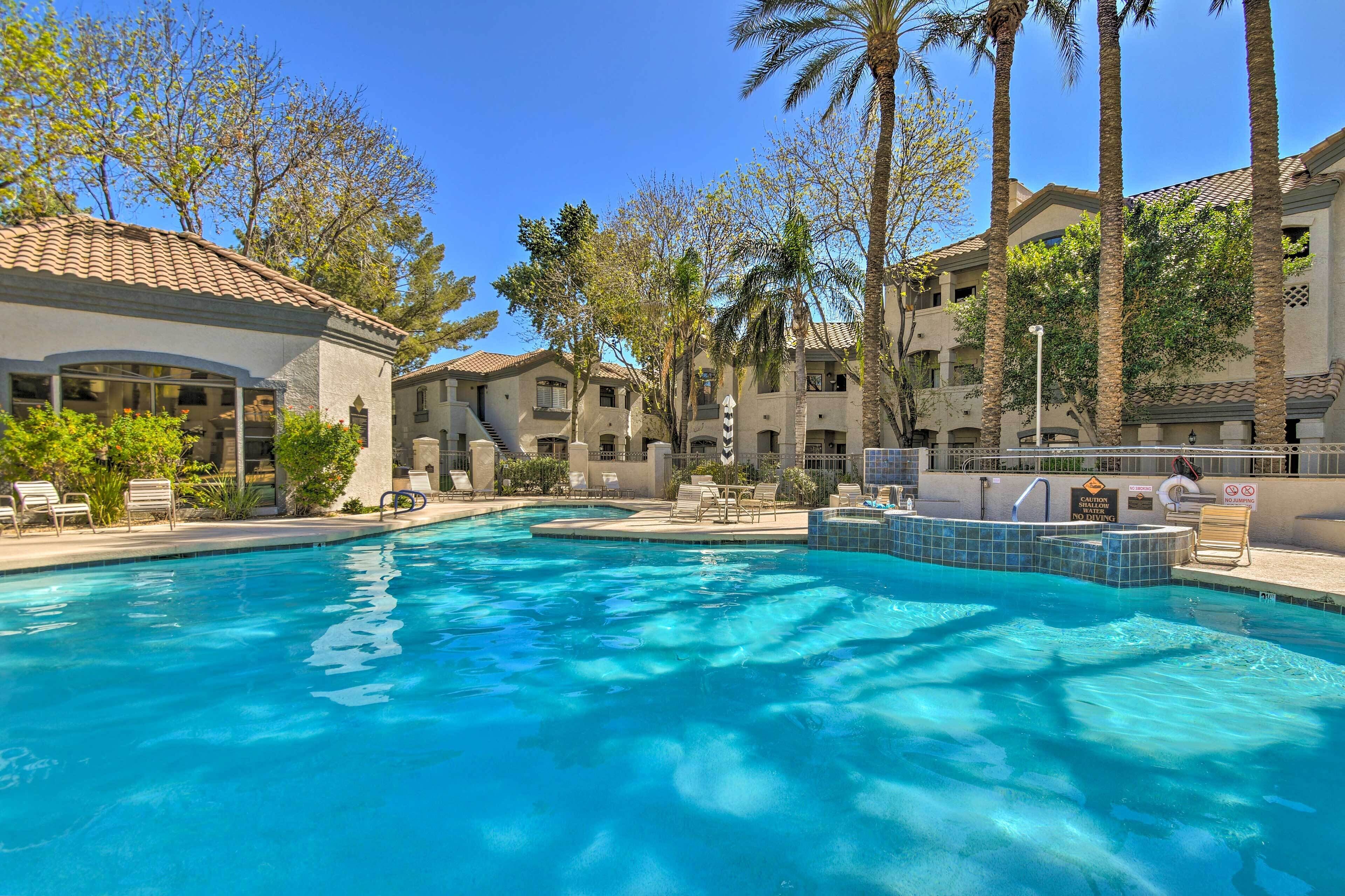 En swimmingpool med liggestole, palmer og en bygning med flere altaner.