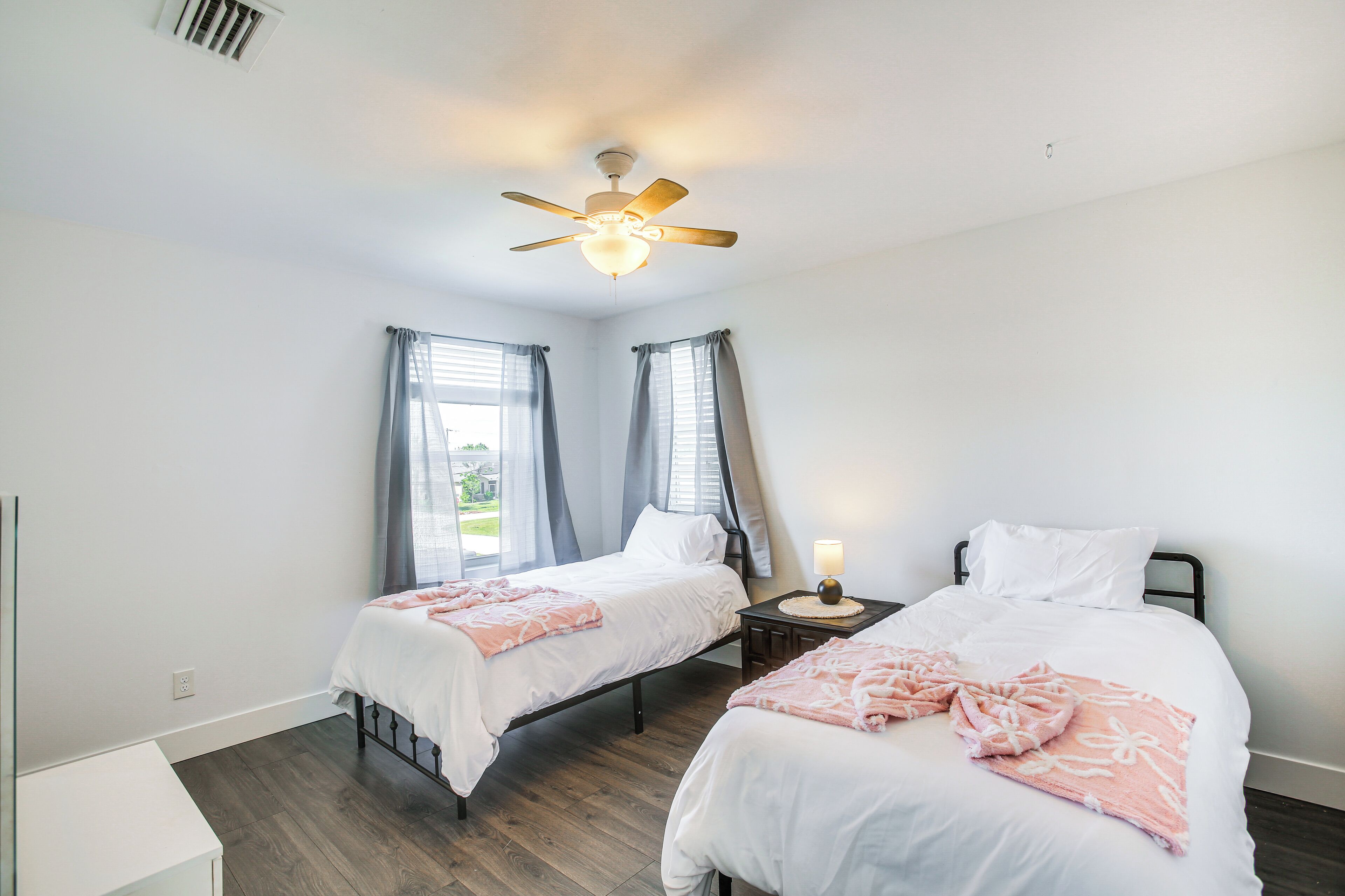 Une chambre avec deux lits, un ventilateur de plafond et une table de chevet avec une lampe.