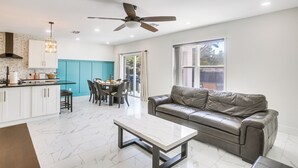 Eine moderne Küche mit weißen Schränken, ein Essbereich mit Tisch und Stühlen, ein Ledersofa und ein Deckenventilator.