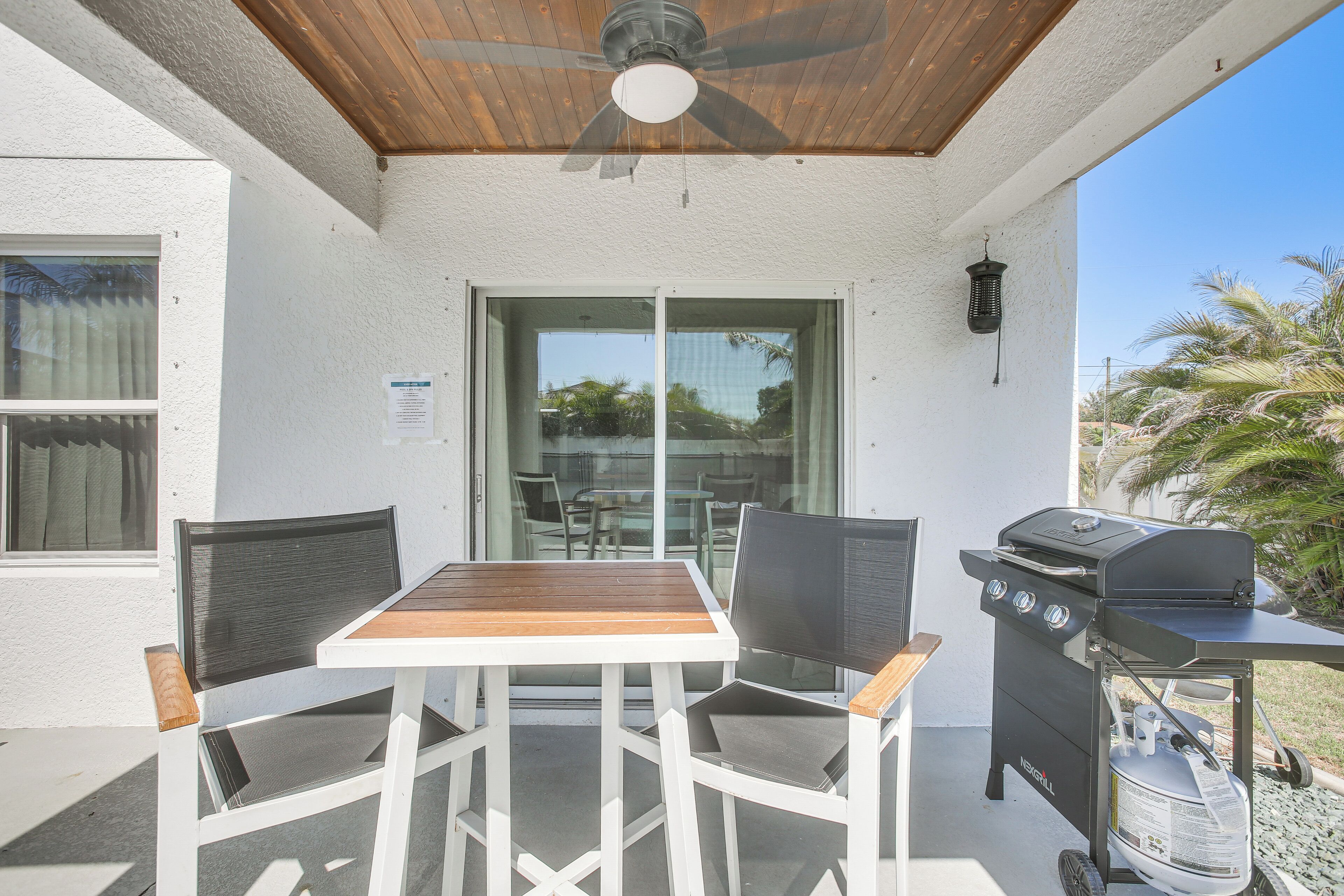 An outdoor patio with a table and chairs, a ceiling fan, and a grill.
