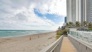 A beach with a wooden boardwalk, tall buildings, and a clear sky.