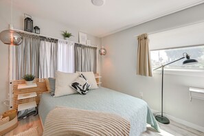Un dormitorio con cama, mesitas de noche, una lámpara de pie, una ventana con cortinas y una estantería con adornos.