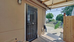 A covered porch with a wooden bench, a black door with a window, and a view of a garden. - 1 Mi to Military Base: Cozy Imperial Beach Studio (Imperial Beach)
