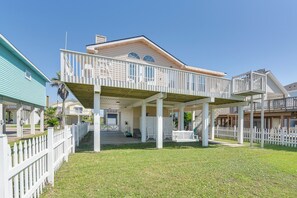 Ein zweistöckiges Haus mit überdachter Veranda, weißem Zaun und blauem Himmel.
