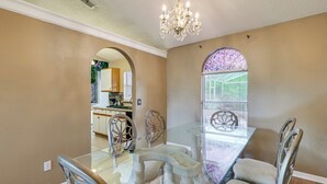 A dining area with a glass table, chairs, a chandelier, and a view of the kitchen through an arched window. - Themed Interior, Poolside Fun! Villa Near Disney (Davenport)
