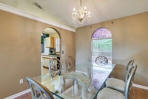 A dining area with a glass table, chairs, a chandelier, and a view of the kitchen through an arched window. - Themed Interior, Poolside Fun! Villa Near Disney (Davenport)