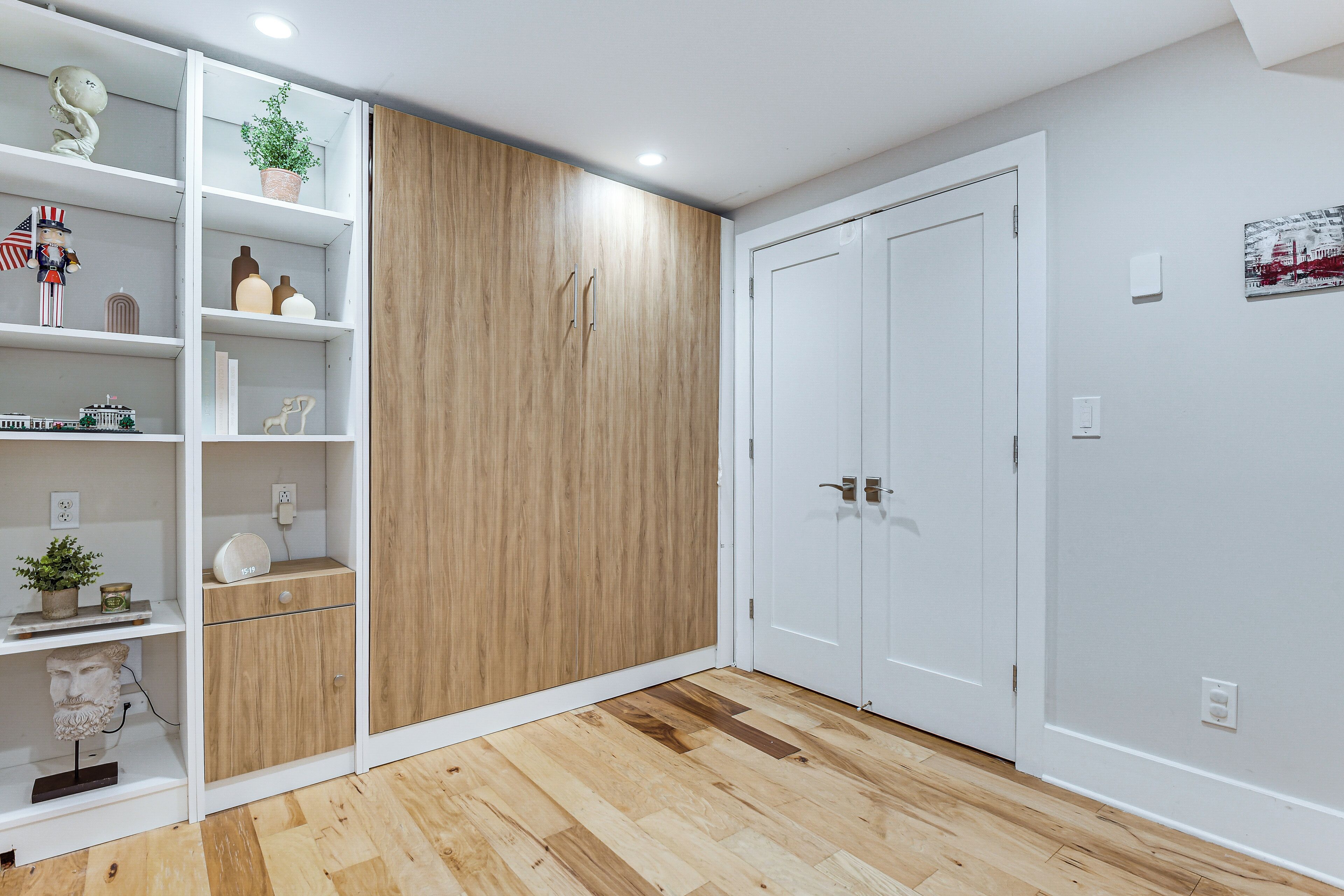 Ein Zimmer mit einem Holzschrank, weißen Regalen mit Dekoration und einer weißen Tür.