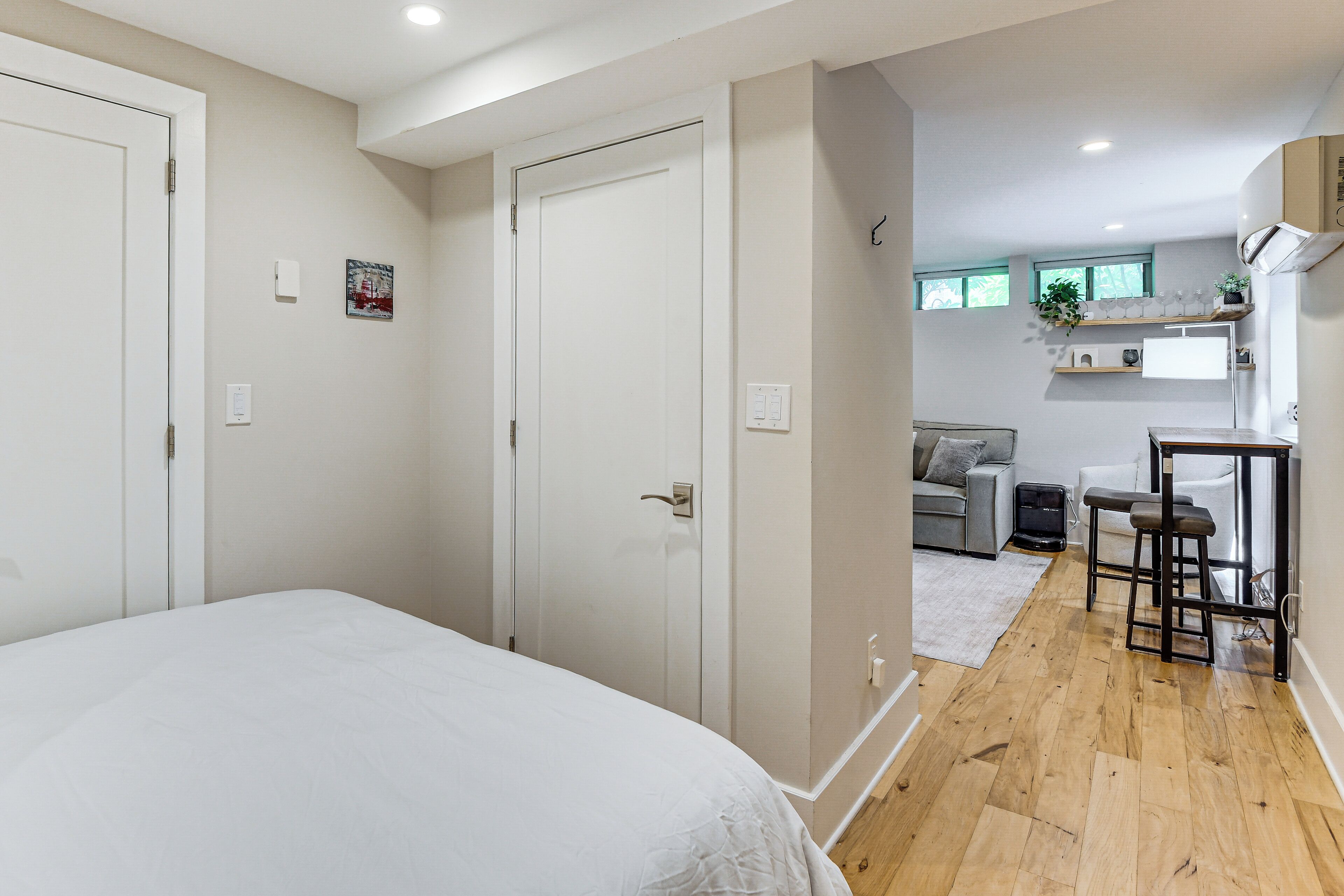 A bedroom with a large bed, a door, and a hallway leading to a kitchenette with a sink, countertop, and stools.