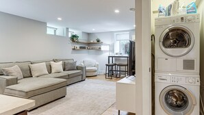 Una sala moderna con un sofá modular, un pequeño comedor y una lavadora de carga frontal.