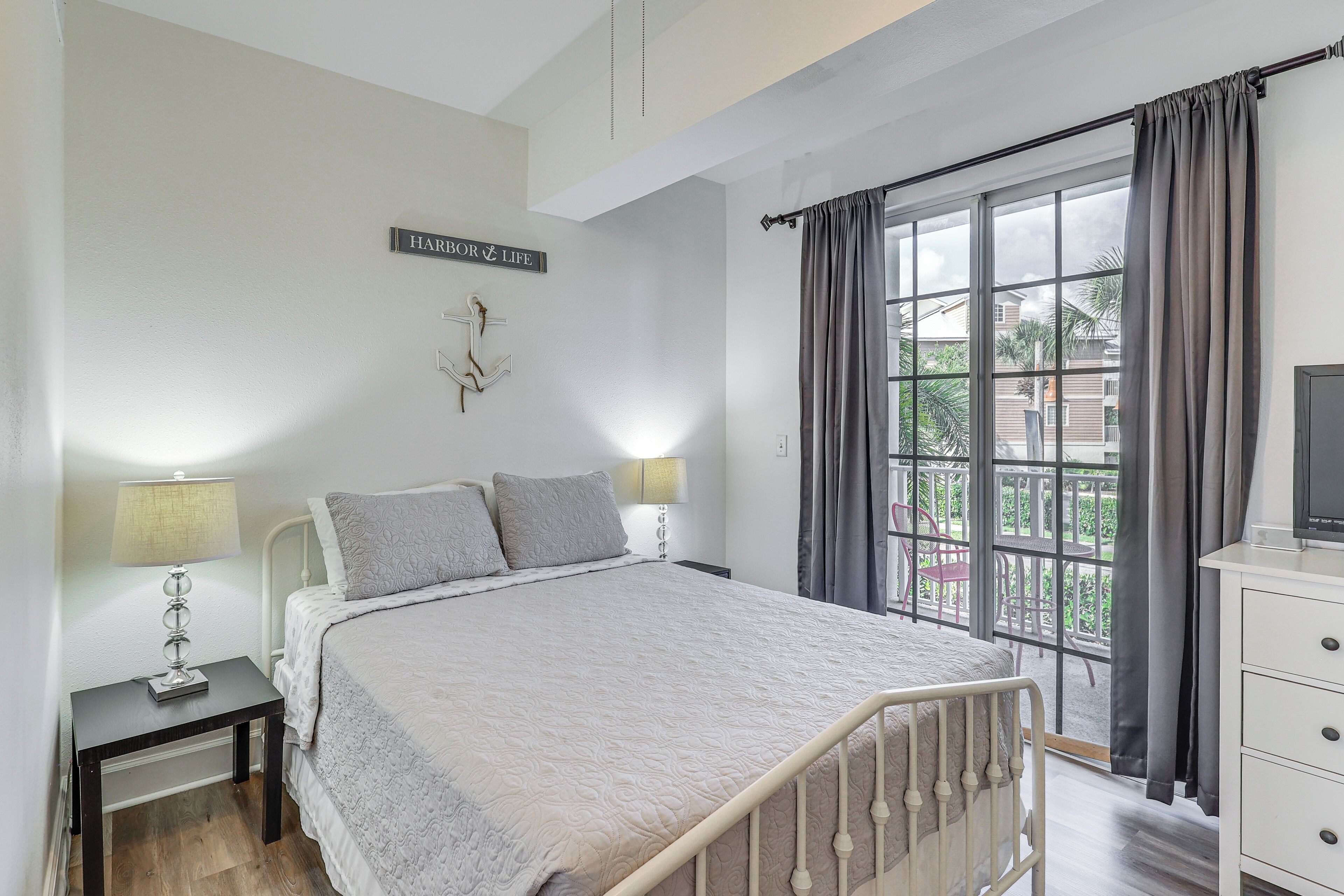 A bedroom with a bed, two bedside tables with lamps, a dresser, a window with curtains, and a sign on the wall.