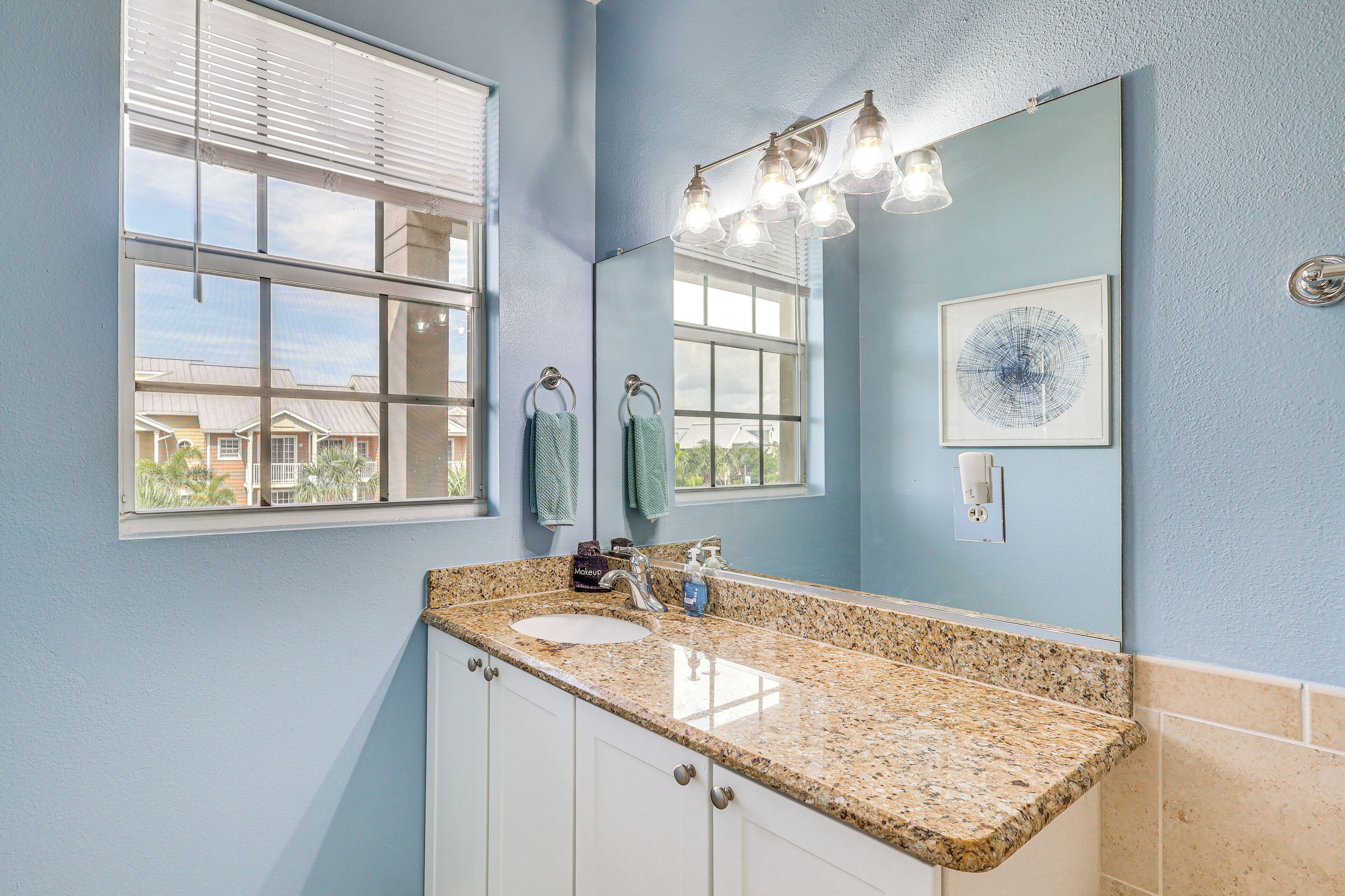 A bathroom with a granite countertop, a sink, a mirror, and a window with blinds.