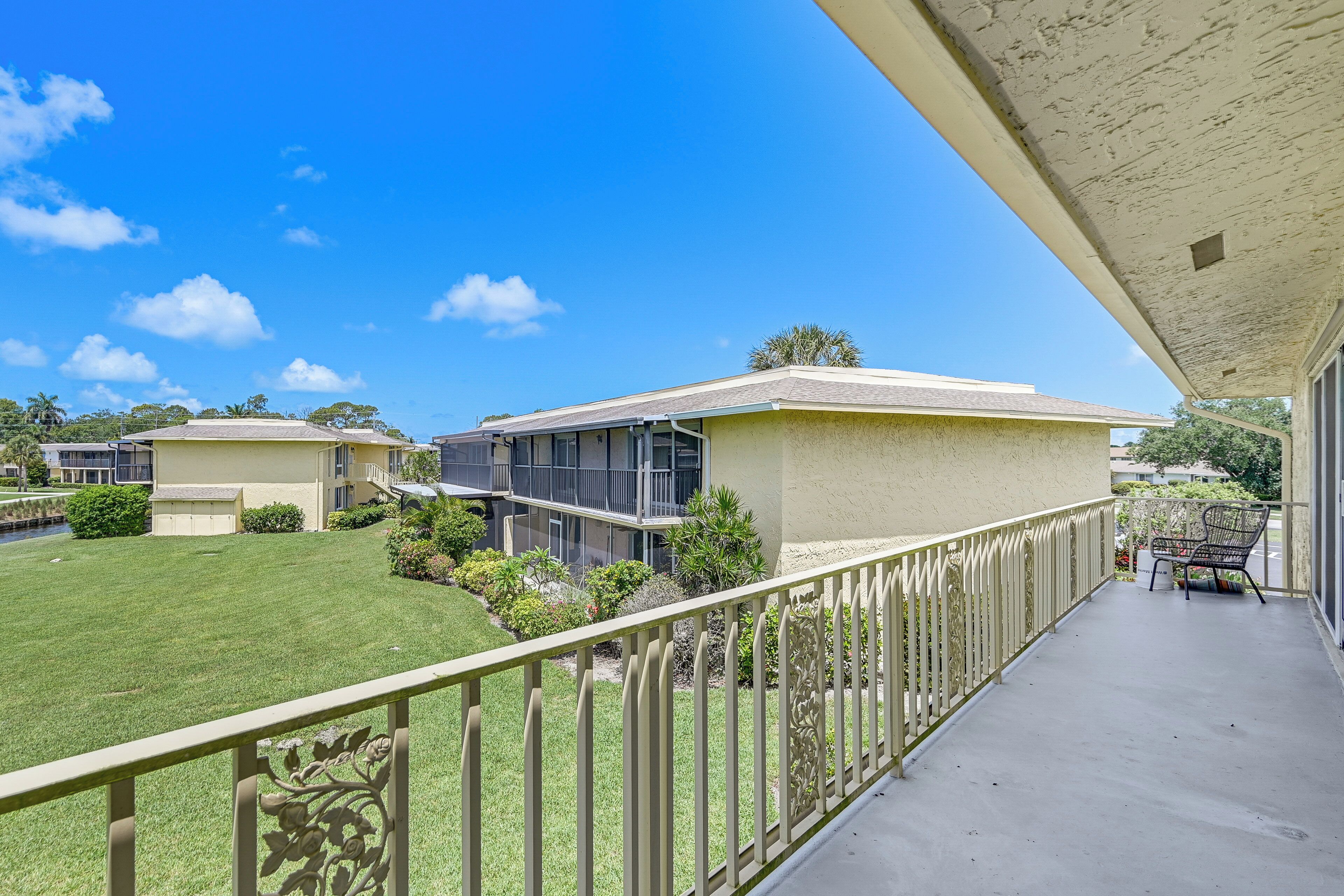 A balcony with a metal railing, a grassy lawn, and a building with a flat roof and large windows.