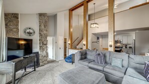 A living room with a grey sofa, a television, a stone wall, and a kitchen in the background. - Ski-in/ski-out! Modern Mountainside Stay in Granby (Granby)