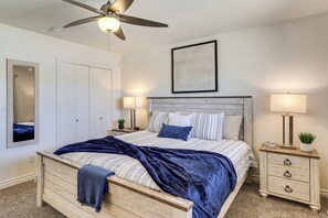 Ein Schlafzimmer mit einem Bett, Nachttischen, einem Deckenventilator, einem Wandbild und einer Tür.