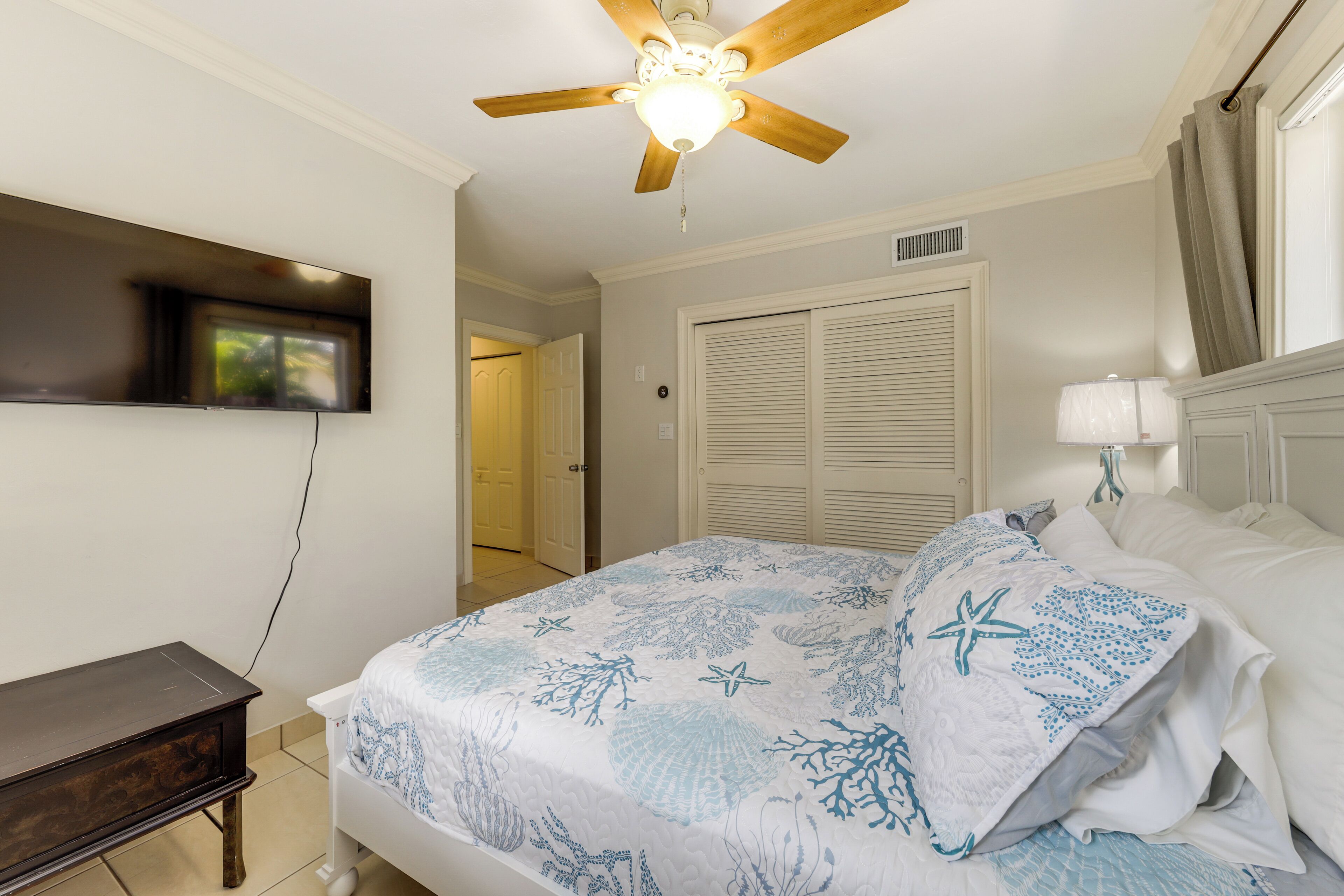 A bedroom with a bed, a ceiling fan, a TV mounted on the wall, and a bedside table.