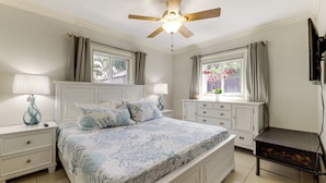 Een slaapkamer met een bed, nachtkastjes, een dressoir, een plafondventilator en een televisie.