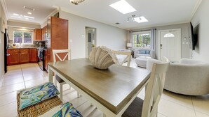 Een moderne keuken met houten kastjes, een eettafel met stoelen en een zithoek met een bank en televisie.