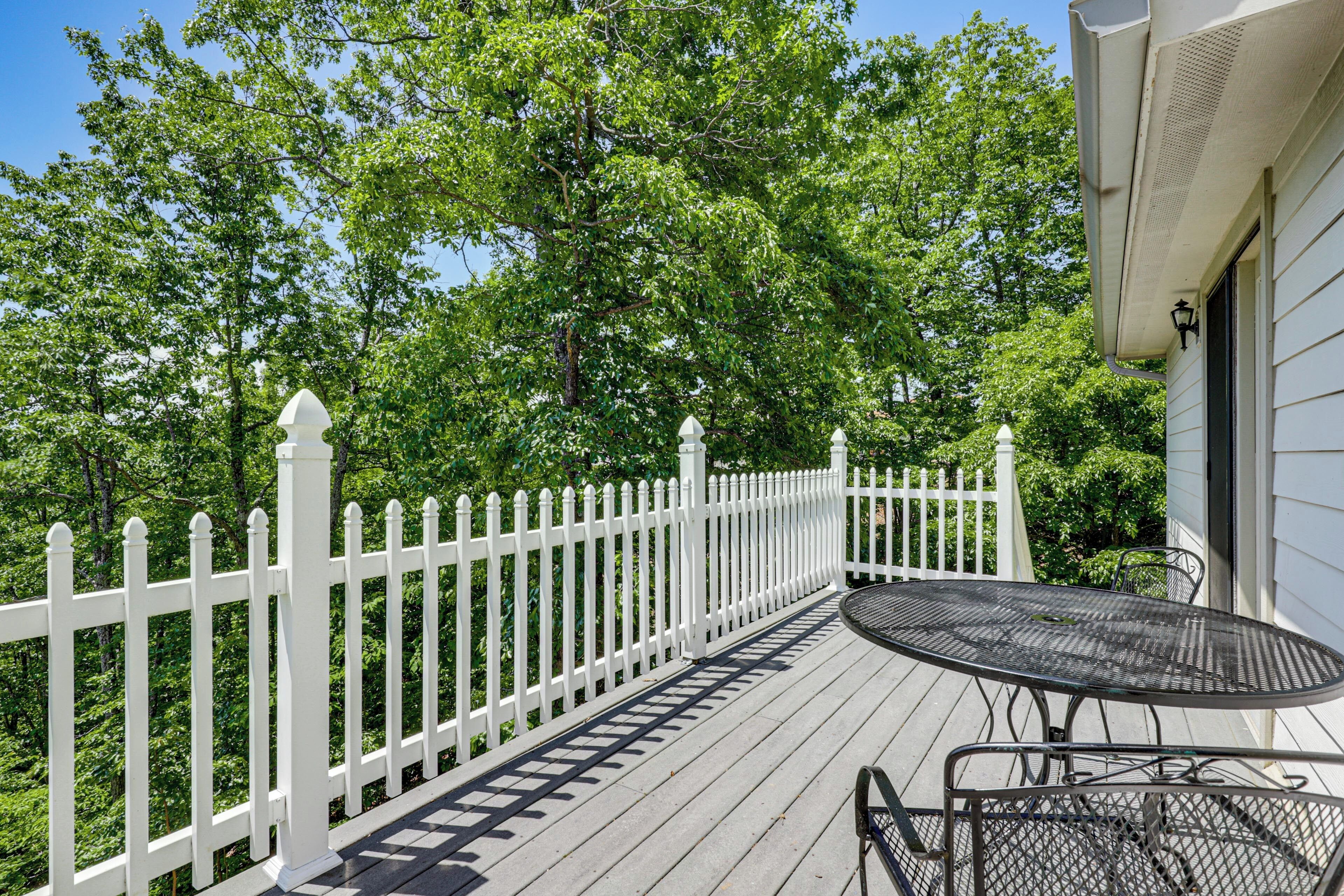 A wooden deck with a white picket fence, a metal table, and chairs.