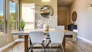 A dining area with a wooden table, white chairs, a vase with white flowers, and a round mirror on the wall. - Pool & Hot Tub Access! Gated Santa Clara Getaway (Santa Clara)