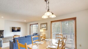 A dining area with a wooden table set for four, surrounded by chairs, with a television and sofa in the background. - Summer Fun! Winter Park Condo w/ Pool, Hot Tub (Winter Park)