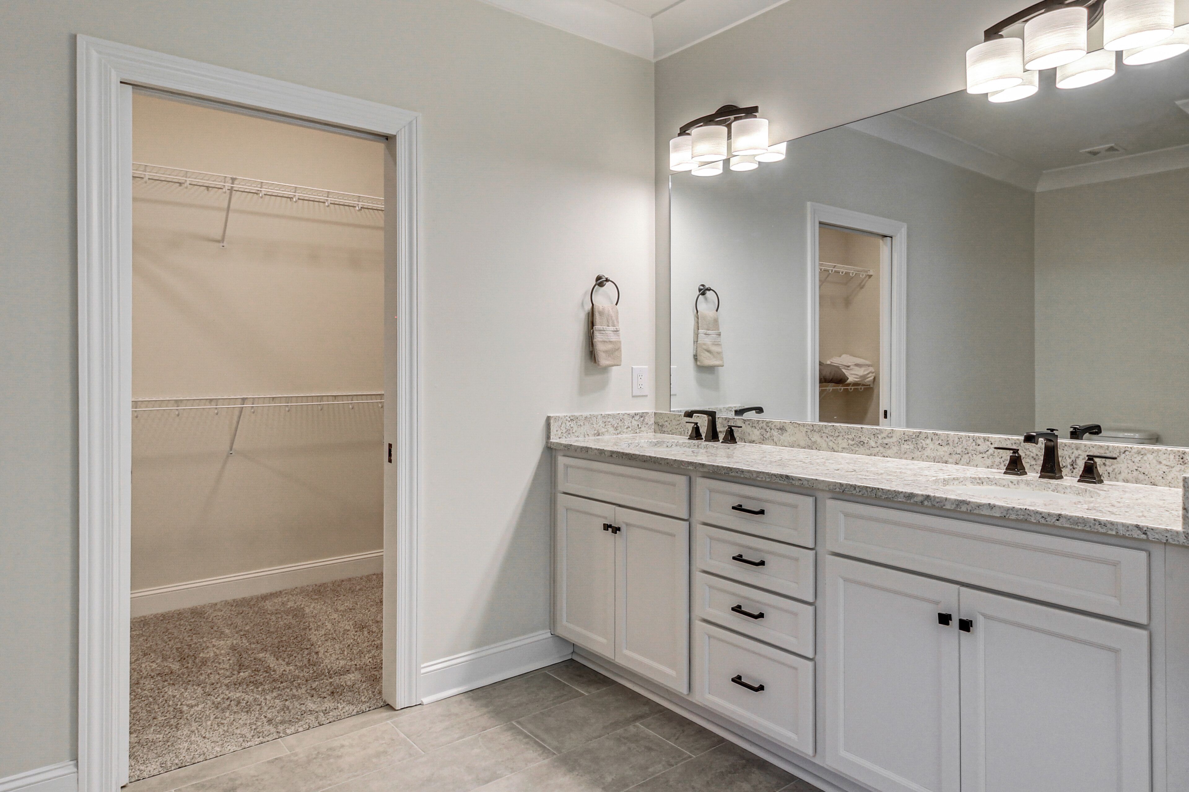 A bathroom with a double sink vanity, a large mirror, and a walk-in closet.
