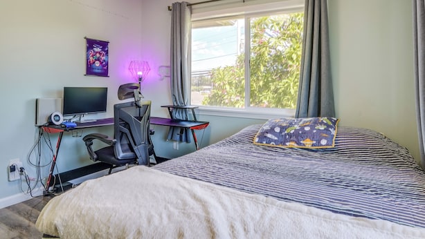 Un dormitorio con una cama, un escritorio con computadora, una silla y un ventanal con cortinas.