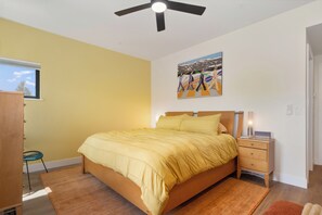 Ein Schlafzimmer mit Bett, Nachttisch, Deckenventilator, Fenster und einem Gemälde an der Wand.