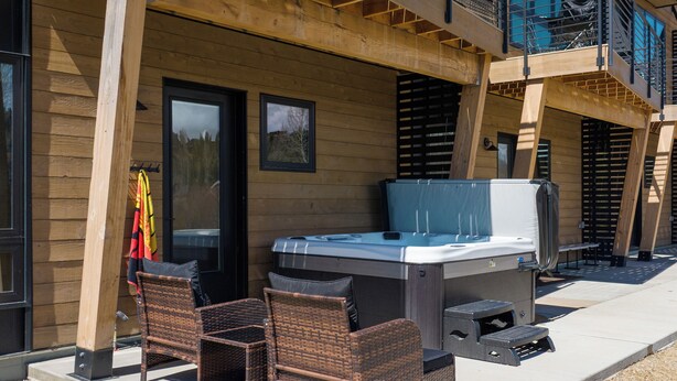 An outdoor patio with a hot tub, wicker chairs, and a wooden deck. - On Fraser River w/ Trail Access! Mtn-view Unit (Fraser)
