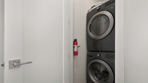 A door with a silver handle, a fire extinguisher mounted on the wall, and a front-loading washer and dryer. - On Fraser River w/ Trail Access! Mtn-view Unit (Fraser)