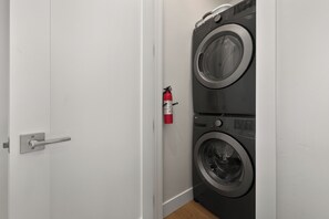 Eine Tür mit silbernem Griff, ein an der Wand befestigter Feuerlöscher sowie eine Waschmaschine und ein Trockner mit Frontlader.