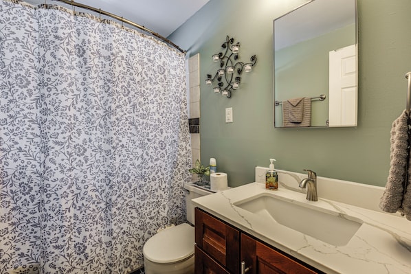 A bathroom with a shower curtain, toilet, sink, mirror, and towel rack.