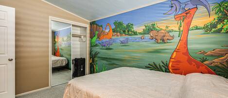 Un dormitorio con un mural de dinosaurios y una cama con colcha color beige.