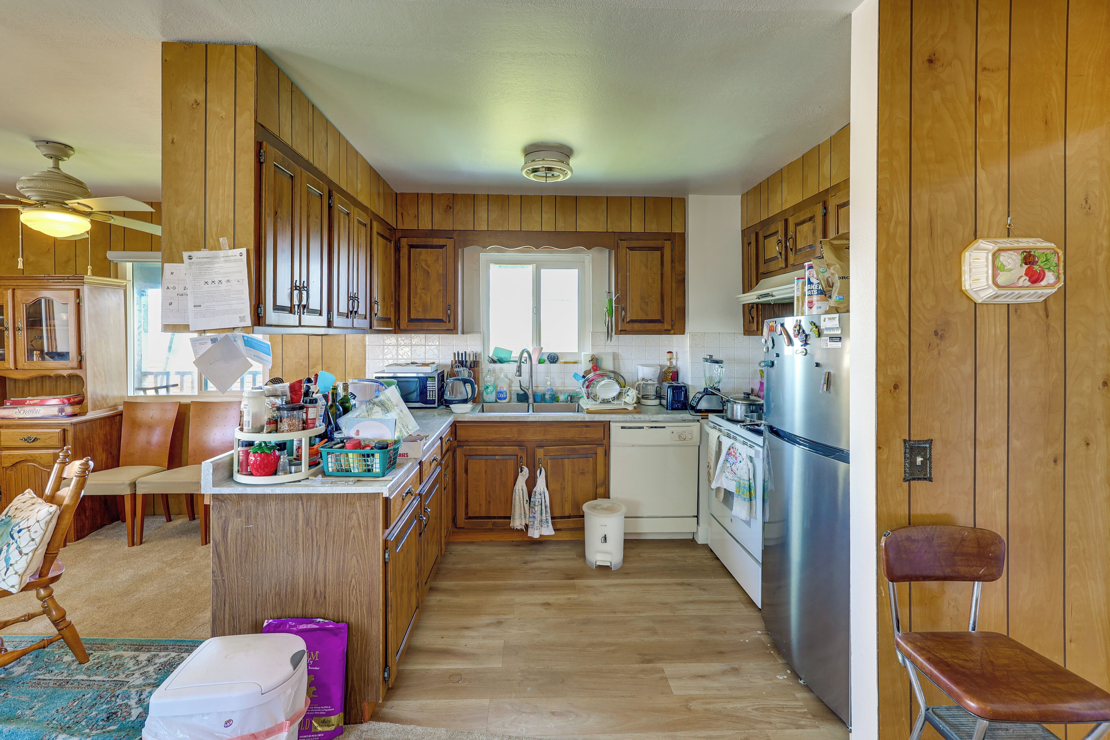 A kitchen with wooden cabinets, a refrigerator, a dishwasher, and a dining area with a chair and table.