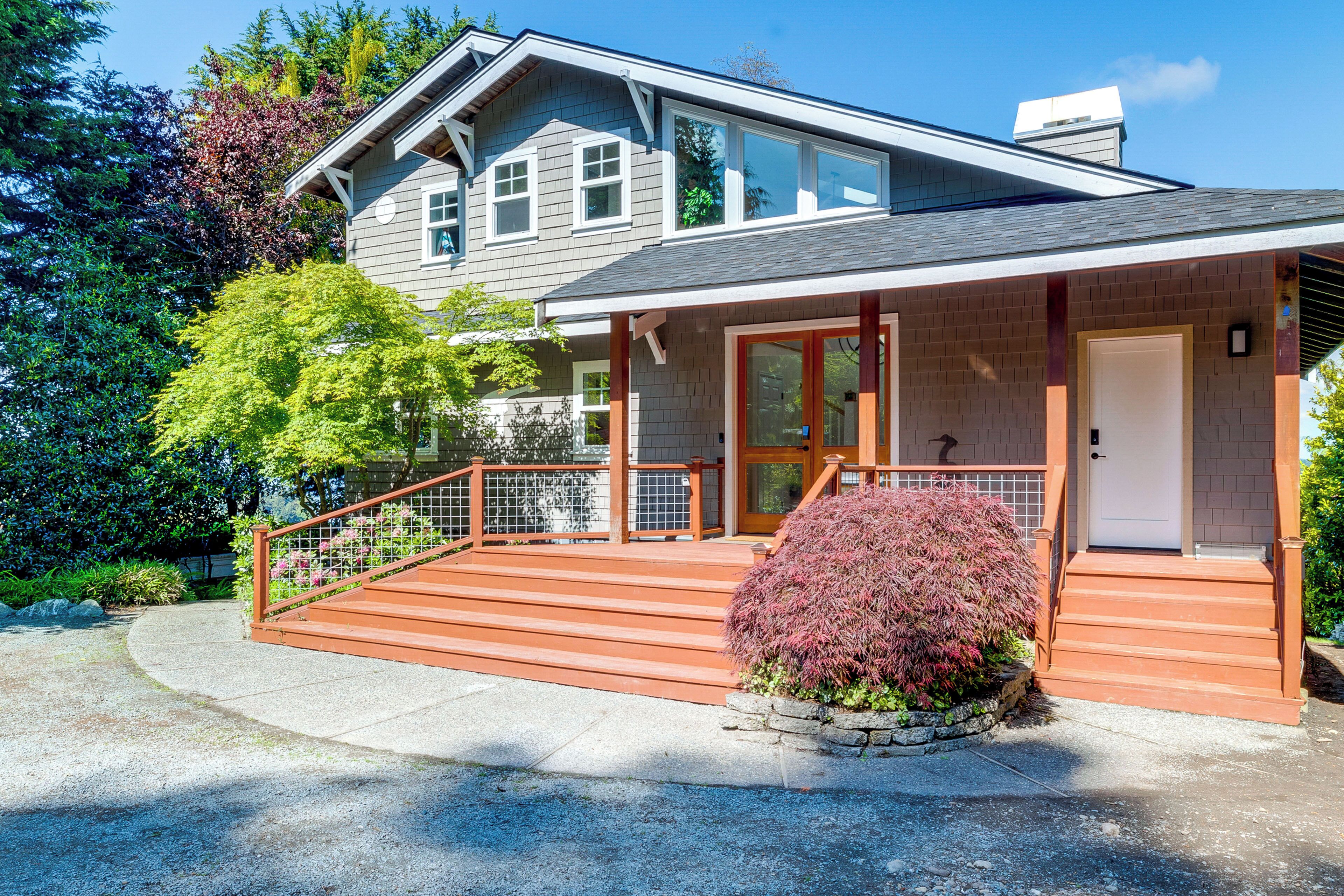A two-story house with a wooden deck, a front door, and a small garden.