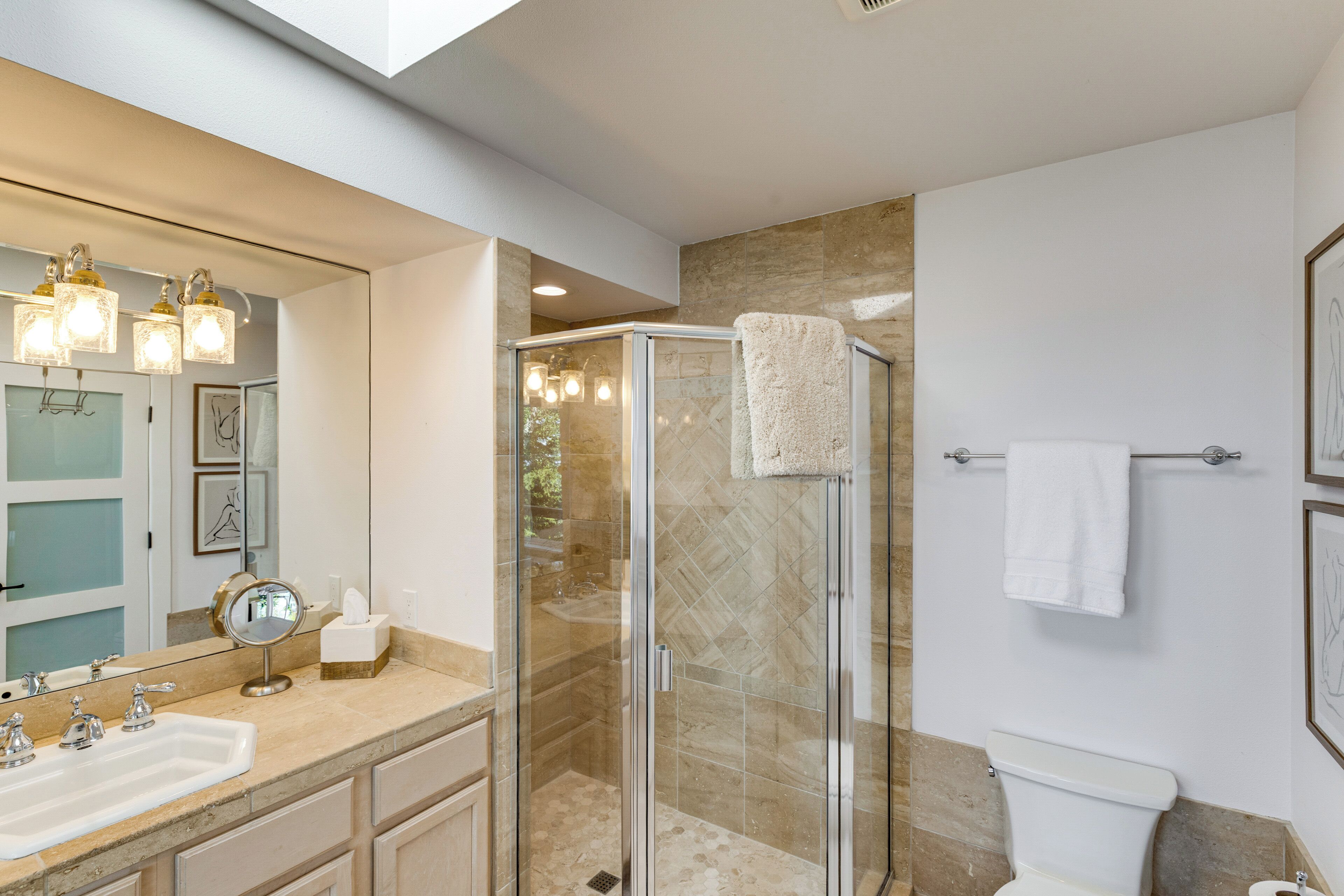 A modern bathroom with a glass-enclosed shower, a large mirror, and a white toilet.