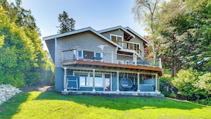 A two-story house with a balcony, a covered porch, and a stone wall. - Snow Goose Point: Stunning Views & New Hot Tub! (Anacortes)
