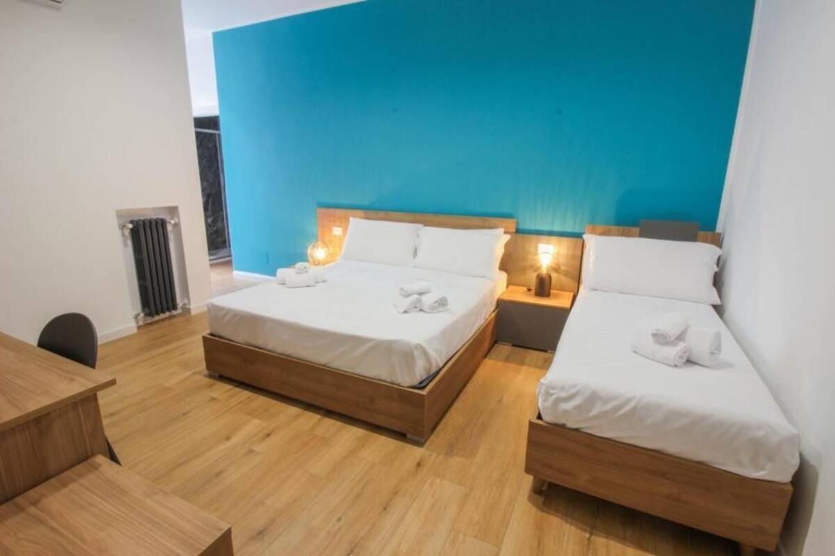 Habitación de hotel con dos camas, un escritorio de madera y una pared azul decorativa.