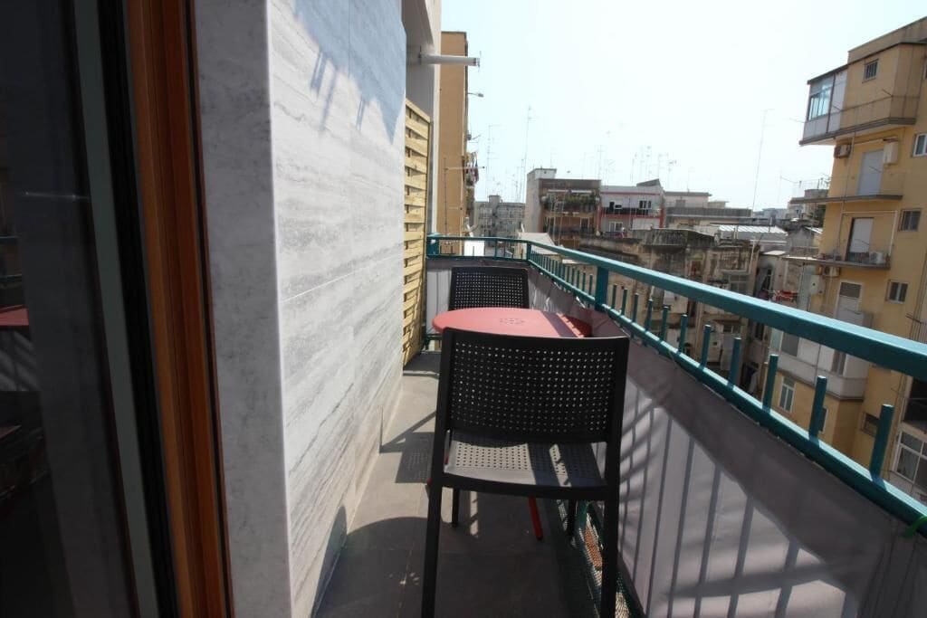 A balcony with a table and chair, overlooking a cityscape with buildings.