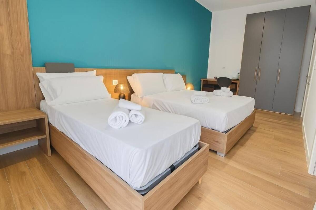 Habitación de hotel con dos camas, cabeceros de madera y una pared de acento color aguamarina.