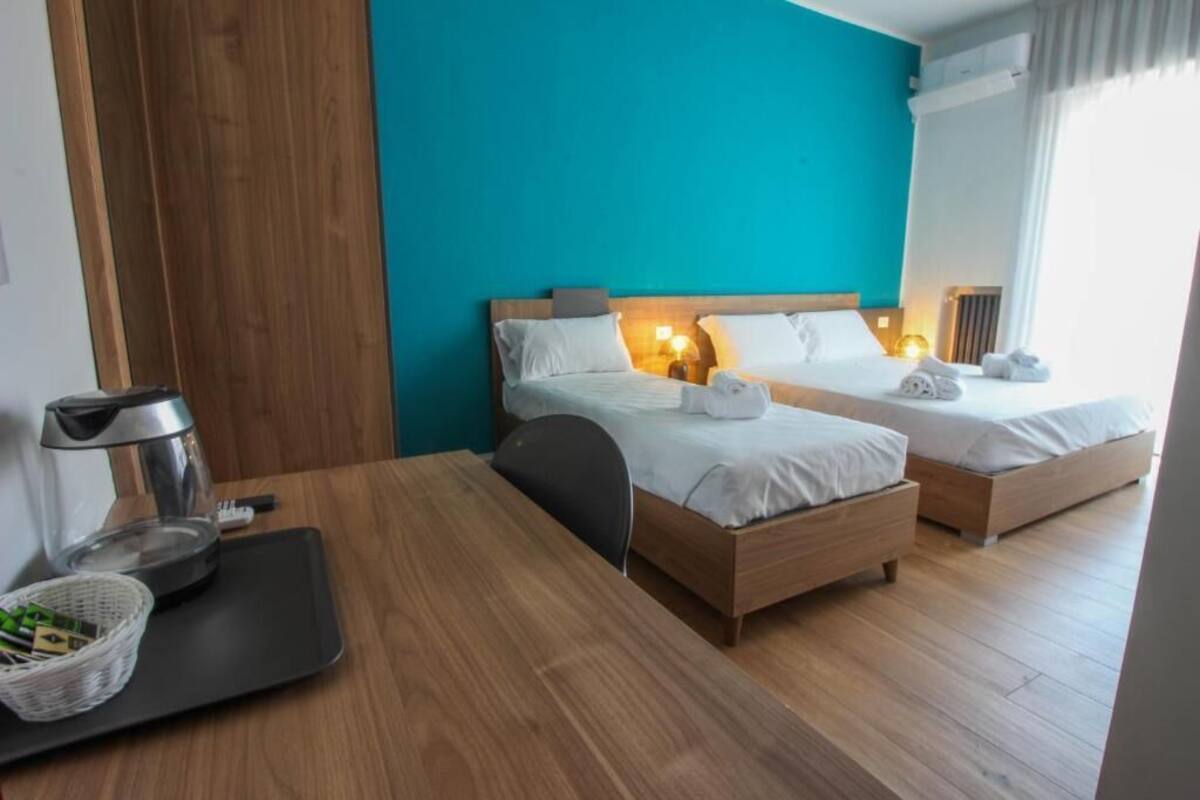 Habitación de hotel con dos camas, una mesa de madera, una cafetera y una cesta de verduras verdes.