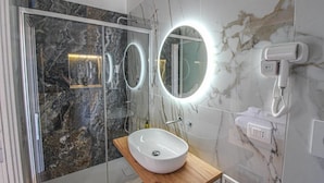 Un baño moderno con cabina de ducha de vidrio, un lavabo blanco sobre una cómoda de madera y un espejo grande con iluminación integrada.