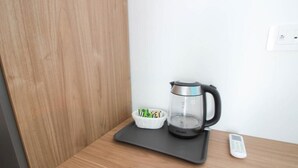 Una cafetera sobre un tapete negro, una cesta con bolsitas de té y un control remoto sobre una mesa de madera.