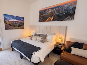 A bedroom with a bed, bedside tables, a nightstand, a couch, and two large landscape paintings on the wall.