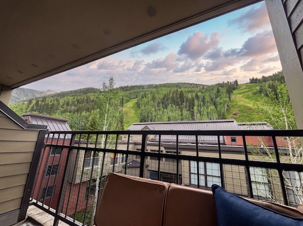 A balcony with a view of a forested hillside and buildings.