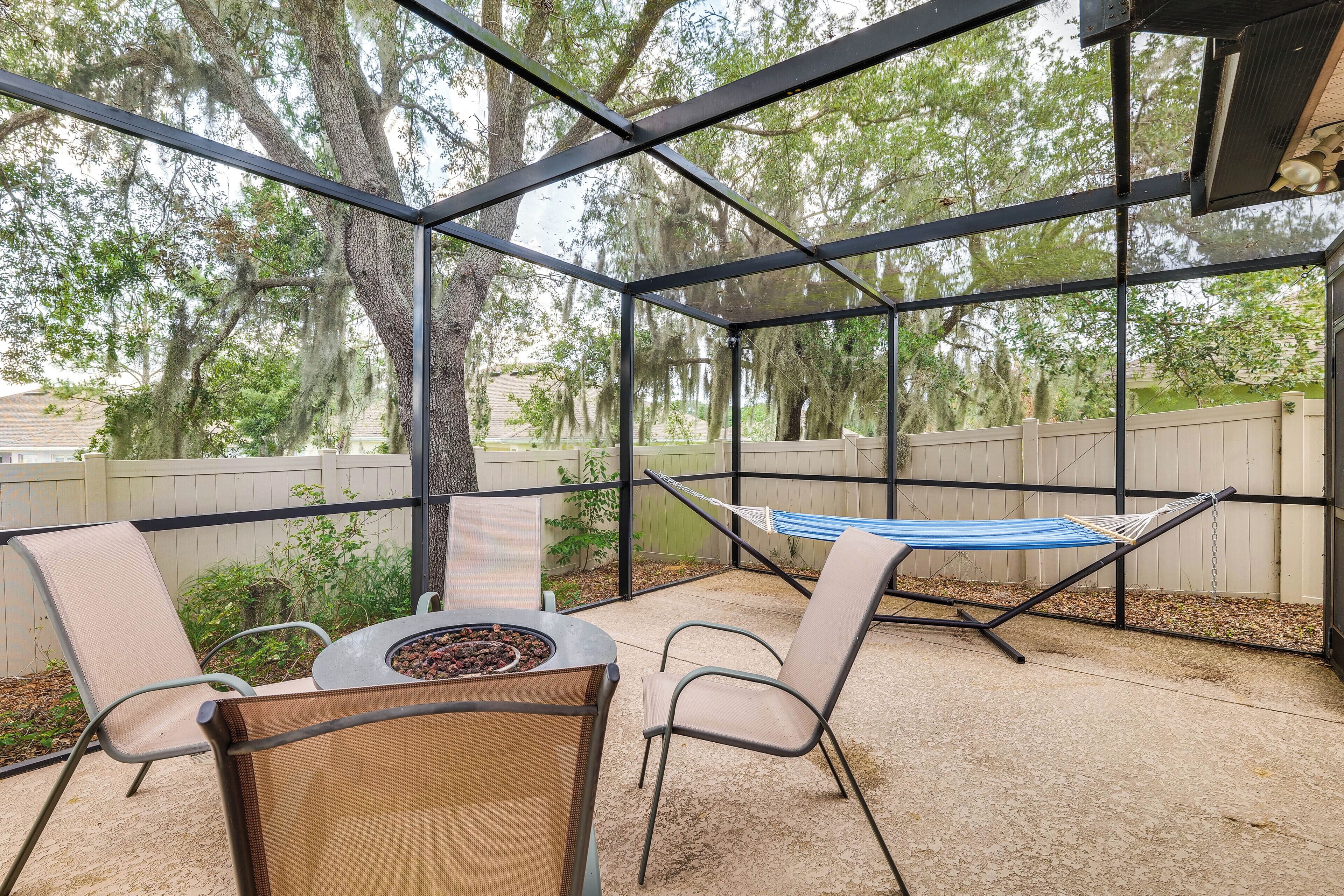 A covered patio with a fire pit, chairs, and a hammock.