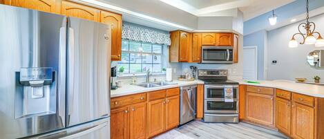 A kitchen with stainless steel appliances, wooden cabinets, a microwave, and a ceiling fan.
