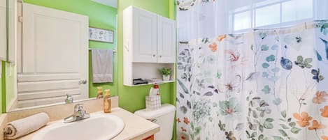 Une salle de bain équipée d’un lavabo, d’un miroir, de toilettes et d’un rideau de douche orné de motifs floraux.